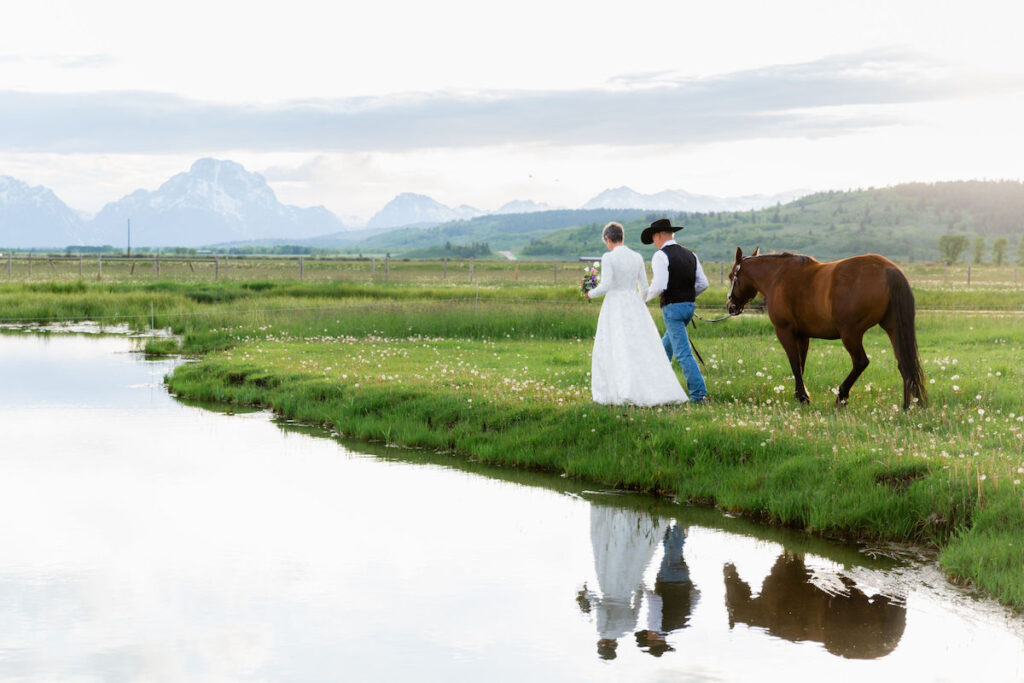 A couple leading a horse, reflected in water, with Mount Moran in the background | Jamye Chrisman | Wyoming Wedding Photographer