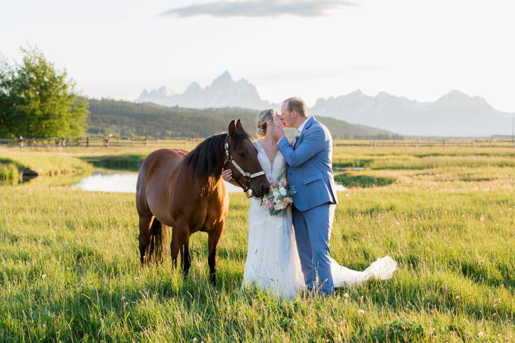 A post-wedding ceremony kiss at golden hour in front of the Teton Range, with Cupcake the horse making an appearance. Jamye Chrisman | Wyoming Wedding Photographer
