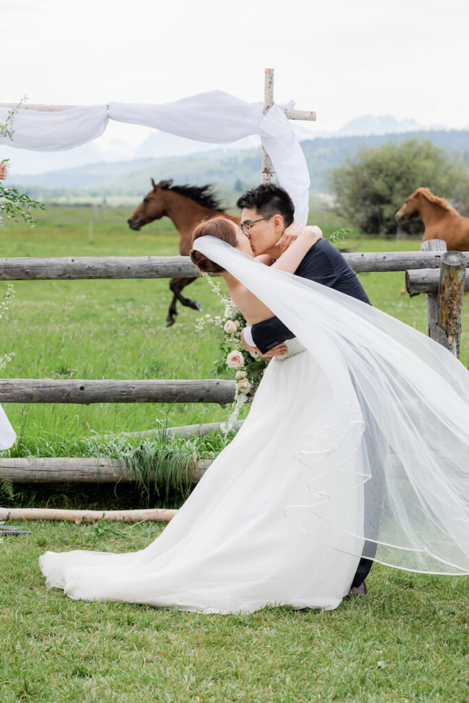 Wedding ceremony first kiss with horses running in the background at Diamond Cross Ranch in Jackson Hole | Jamye Chrisman | Wyoming Wedding Photographer