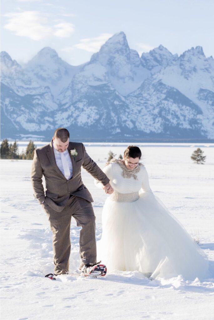 A happy couple snowshoes away from the Grand Teton during their winter wedding photoshoot | Jamye Chrisman | Jackson Hole Wedding Photographer