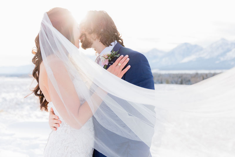A bride and groom kiss in the Tetons during their winter wedding photo session by Jamye Chrisman