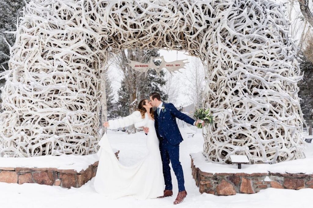 A couple kisses under the elk antler arch in the winter on the Town Square in Jackson Hole Wyoming